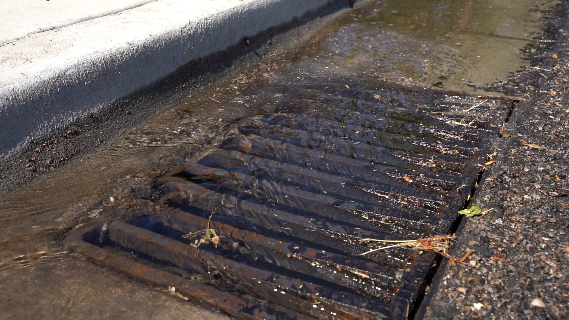 Storm drain between the sidewalk and street with water flowing into it