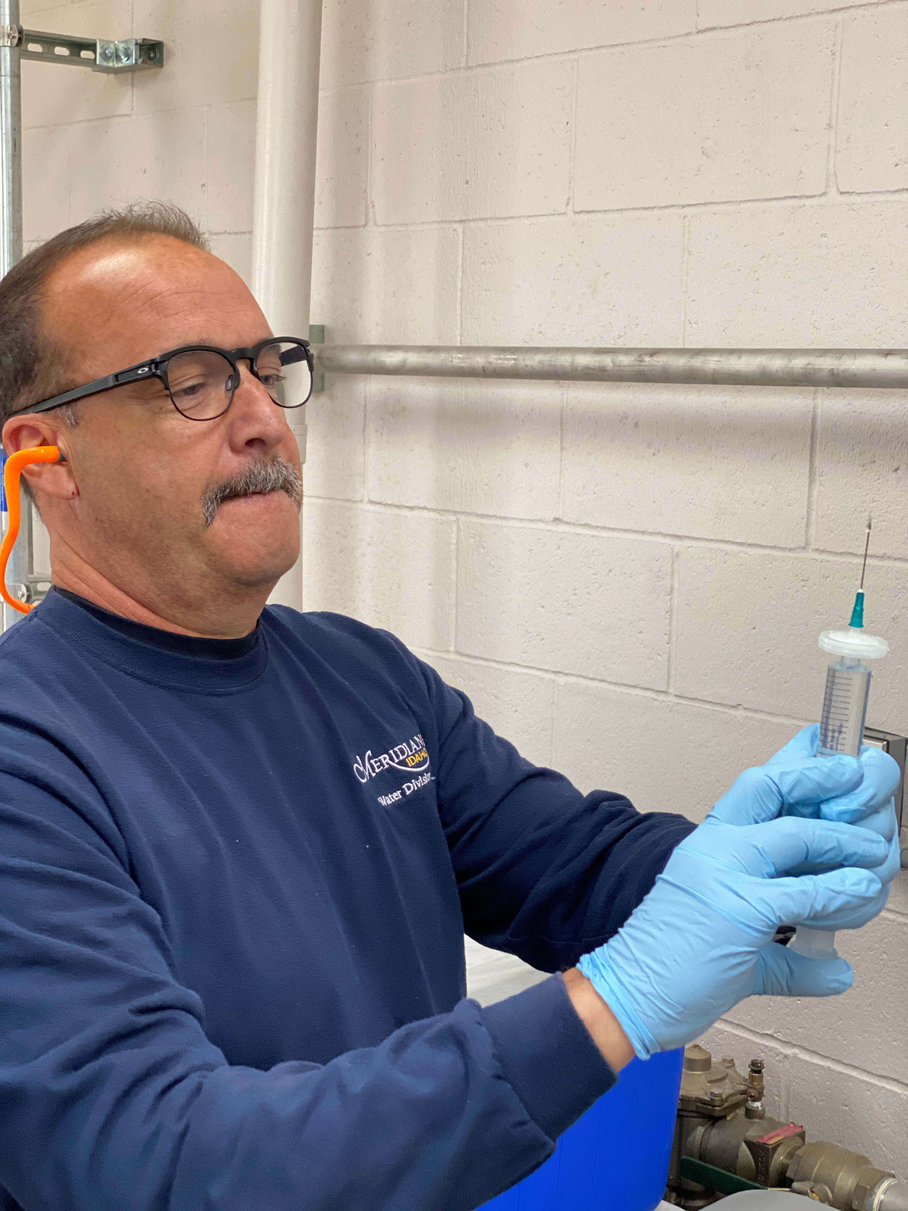 Water Quality Specialist, wearing gloves and ear plugs, holding a tube of water with a syringe looking tip